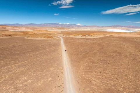 Aerial shot of a lone car on an endless desert road under a blue sky in the argentine Puna. The