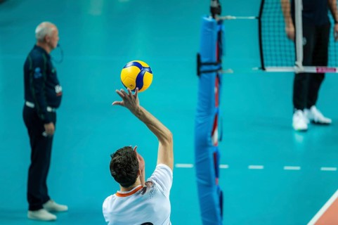 Volleyball player sreves ball, referee in the background.