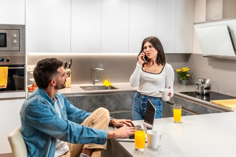 Young couple working remotely in their modern kitchen, enjoying breakfast while managing their