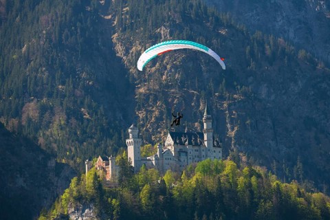 A paraglider flies over Neuschwanstein Castle against a mountain backdrop, Schwangau near Füssen,