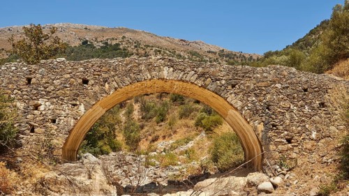 Old stone bridge in front of a mountain panorama with dry terrain under clear sky, Amari Basin,