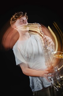 A teenage boy plays a saxophone with dynamic motion blur against a black studio background,