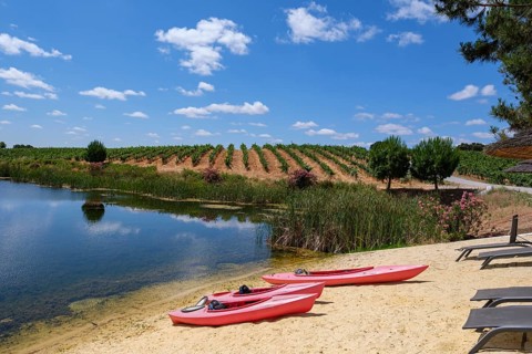 Two red kayaks lie on the sandy shore of a clear lake under a blue sky, Pedrógão, Beja, Portugal