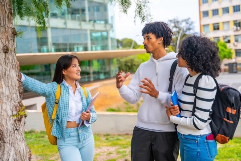 Three multi-ethnic friends talking leaning on a tree in the university