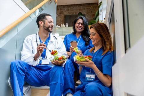 Healthcare professionals sharing a happy moment and eating salads during their lunch break at a