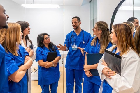 Healthcare professionals in scrubs and lab coats actively listening to a male doctor, sharing