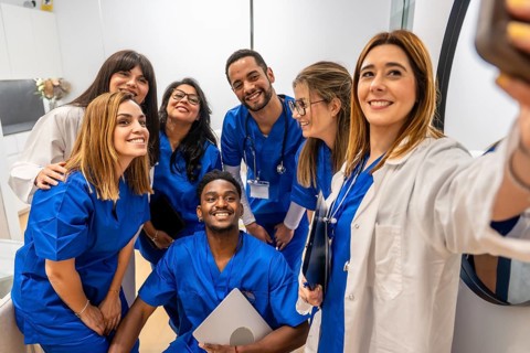 Diverse smiling healthcare team of doctors and nurses in scrubs and lab coats posing for a cheerful