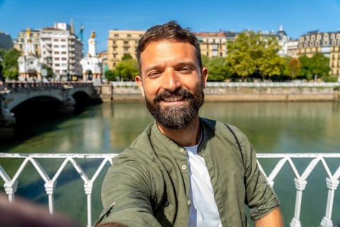Smiling bearded man takes a selfie on maria cristina bridge over the urumea river, enjoying a sunny