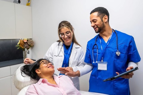 Diverse medical team internist and scrub clad clinician warmly engaging a smiling female patient