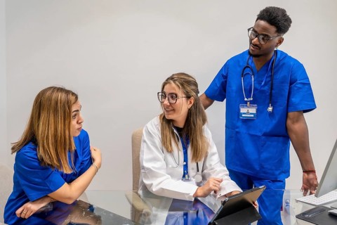 Medical team of doctor and nurses collaborating at a desk, using tablet and computer while
