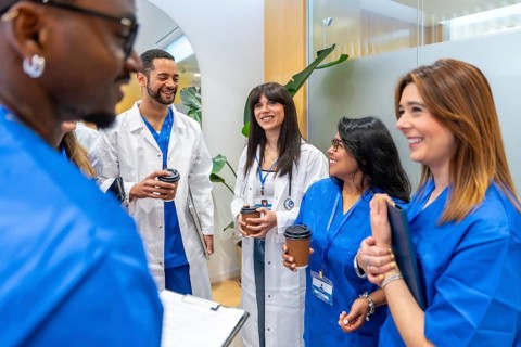 Medical staff, including doctors and nurses, smiling and discussing while holding coffee cups