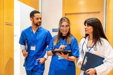 Healthcare professionals walk down a hospital corridor, consulting a digital tablet and clipboard