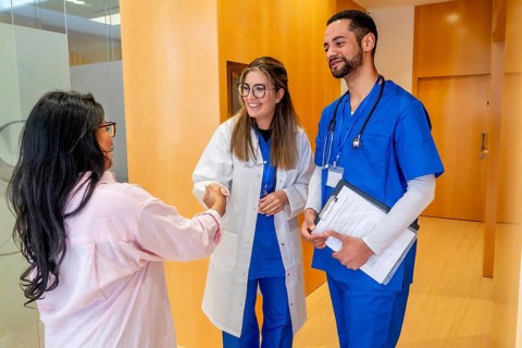 Female doctor in lab coat and male nurse in scrubs warmly greet a female patient with a handshake