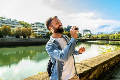 Happy young man enjoying music and singing along using his smartphone as a microphone and wearing