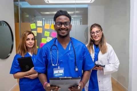 Diverse medical team in a modern clinic, smiling doctor with clipboard stands between two female