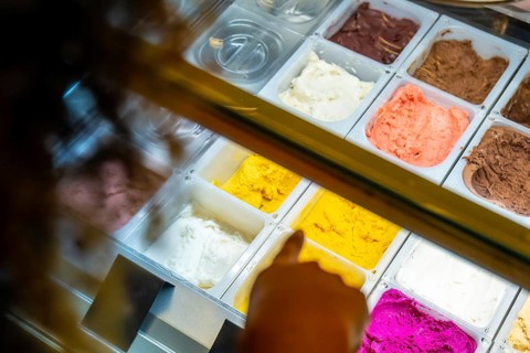 Customer hand pointing at brightly colored gelato and sorbet flavors in a refrigerated display