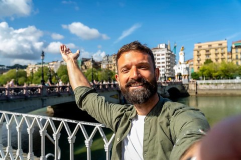 Happy bearded man smiling and taking a selfie portrait during a sunny day trip, enjoying travel and