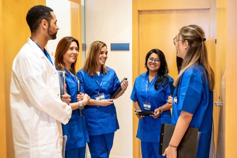 Diverse healthcare team of doctors and nurses in scrubs and a lab coat chatting and smiling in a