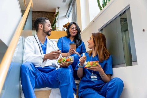 Multiracial medical team colleagues sitting on a staircase, enjoying their healthy lunch during a