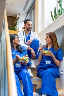 Diverse medical team in scrubs and a lab coat sitting on a staircase in a modern clinic, smiling