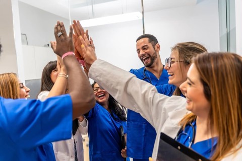 Diverse medical team of happy doctors and nurses stacking hands in a high five gesture, celebrating