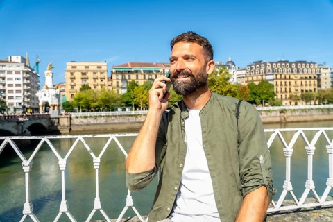 Smiling man talking on his smartphone on maria cristina bridge, enjoying sunny views over the