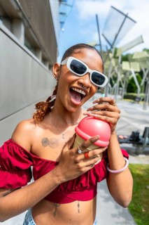 Young woman wearing sunglasses and a red off shoulder top, holding a novelty ice cream cone shaped