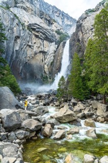 Hiker in yellow jacket enjoying the powerful lower yosemite falls cascading down granite cliffs,