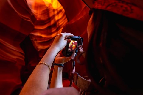 Woman photographing the illuminated, flowing sandstone walls of antelope canyon, capturing the