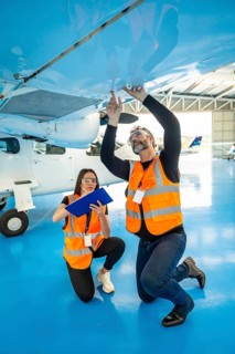 Aviation engineers with safety vests and glasses inspecting an airplane wing in a hangar, one