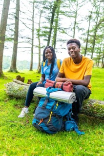 Vertical portrait of two young male and female african friends smiling while sitting on a log in a