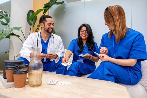 Group of smiling doctors and nurses in blue scrubs and white lab coat engaging in a casual card