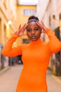 Fashionable urban style with a black African girl in an orange dress and black heels on a city