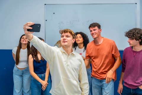 Young diverse students smiling and posing for a smartphone selfie in a bright classroom, capturing