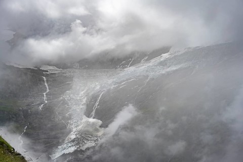 Dramatic mountain landscape covered in clouds, waterfalls and Grindelwald-Fiescherfirn glacier