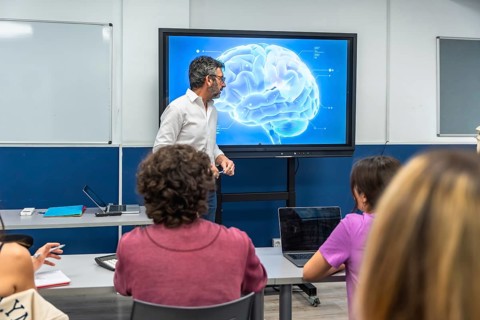 Professor using an interactive screen to present a detailed brain model, explaining neuroscience