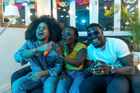 Excited multi-ethnic young friends singing karaoke together during night party at home