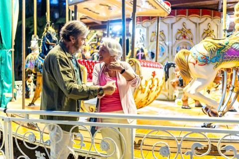 Senior man and woman enjoying ride in an old-fashion carousel standing chatting aside