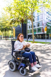 Happy woman wearing glasses, using an electric wheelchair and enjoying a sunny day while exploring