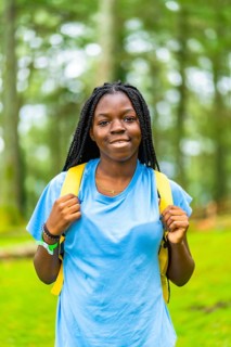 Vertical portrait of a joyful african female backpacker with braided hair enjoying adventure in