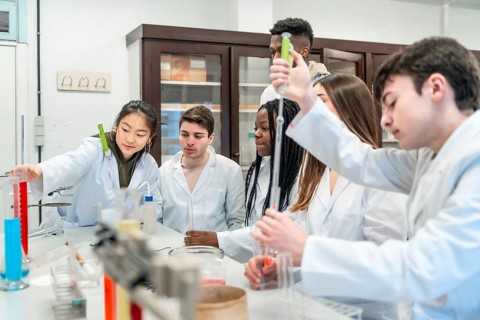 University students in lab coats conducting a chemistry experiment using colorful liquids and lab