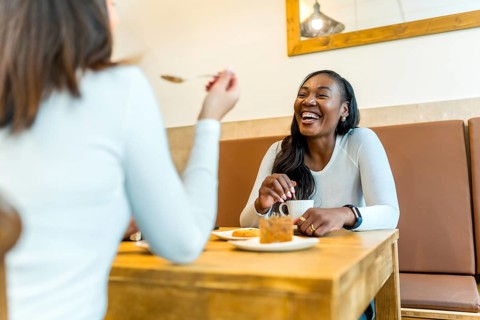 Two women enjoying a relaxing afternoon, sharing coffee and cake while laughing together at a cozy