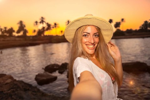 Personal point of view of a woman with straw hat smiling while taking selfie on beach during