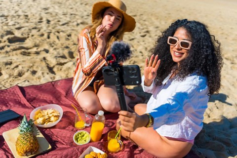 Diverse young female friends creating video content for social media, smiling and waving to a
