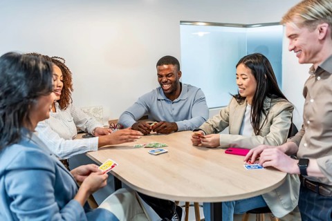 Happy multi ethnic coworkers playing cards at the office desk during a break, enjoying some leisure