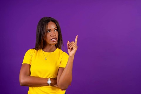 Studio portrait with purple background of a modern african woman looking up and pointing with