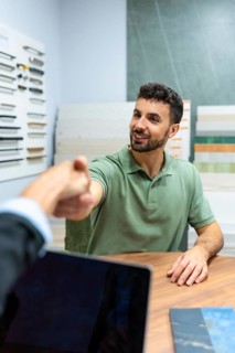 Young man smiling and shaking hands with sales manager in a modern decor showroom, sealing a home