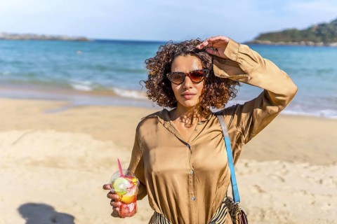 Arab beauty woman eating fresh fruit standing with sunglasses and casual clothes on a beach