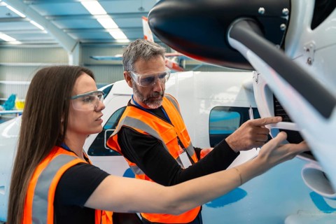 Two aerospace engineers wearing safety vests and goggles, carefully examining an airplane engine