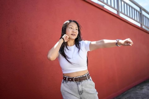 Asian female young urban dancer shadowboxing while dancing K-pop choreography outdoors against a